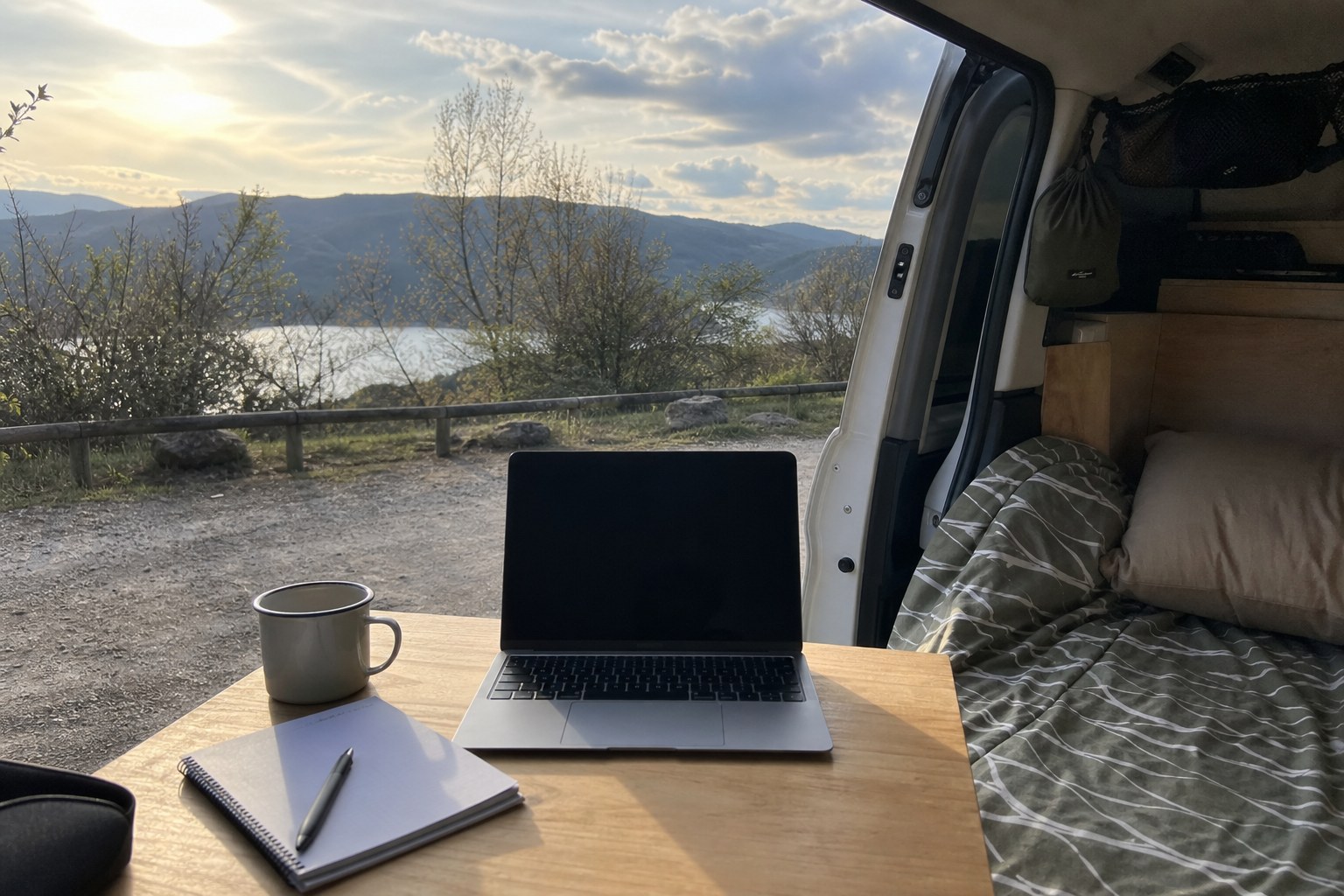 Ordinateur, carnet et tasse dans un van ouvert sur un paysage naturel